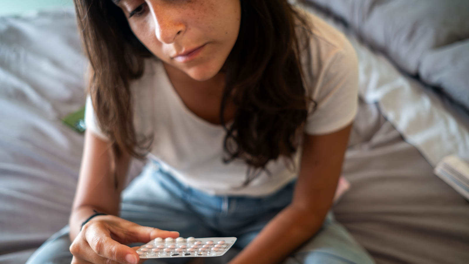 Woman holding Birth Control pills on Bed