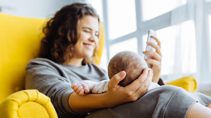 woman looking at her phone while holding her young baby