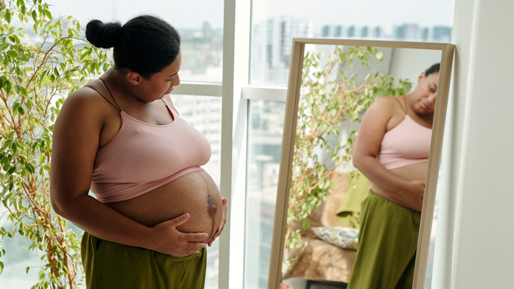 pregnant woman wearing a bra and pants looking at her bump in the mirror