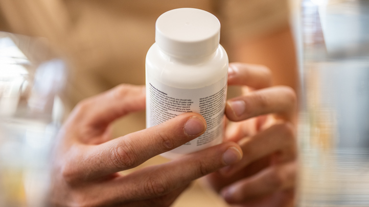 A person is holding a white pill bottle and reading the label on it