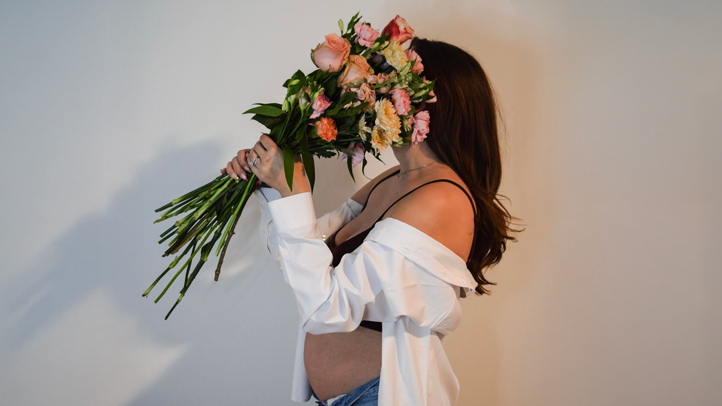 pregnant mom holding a bouquet of pink flowers up to her face